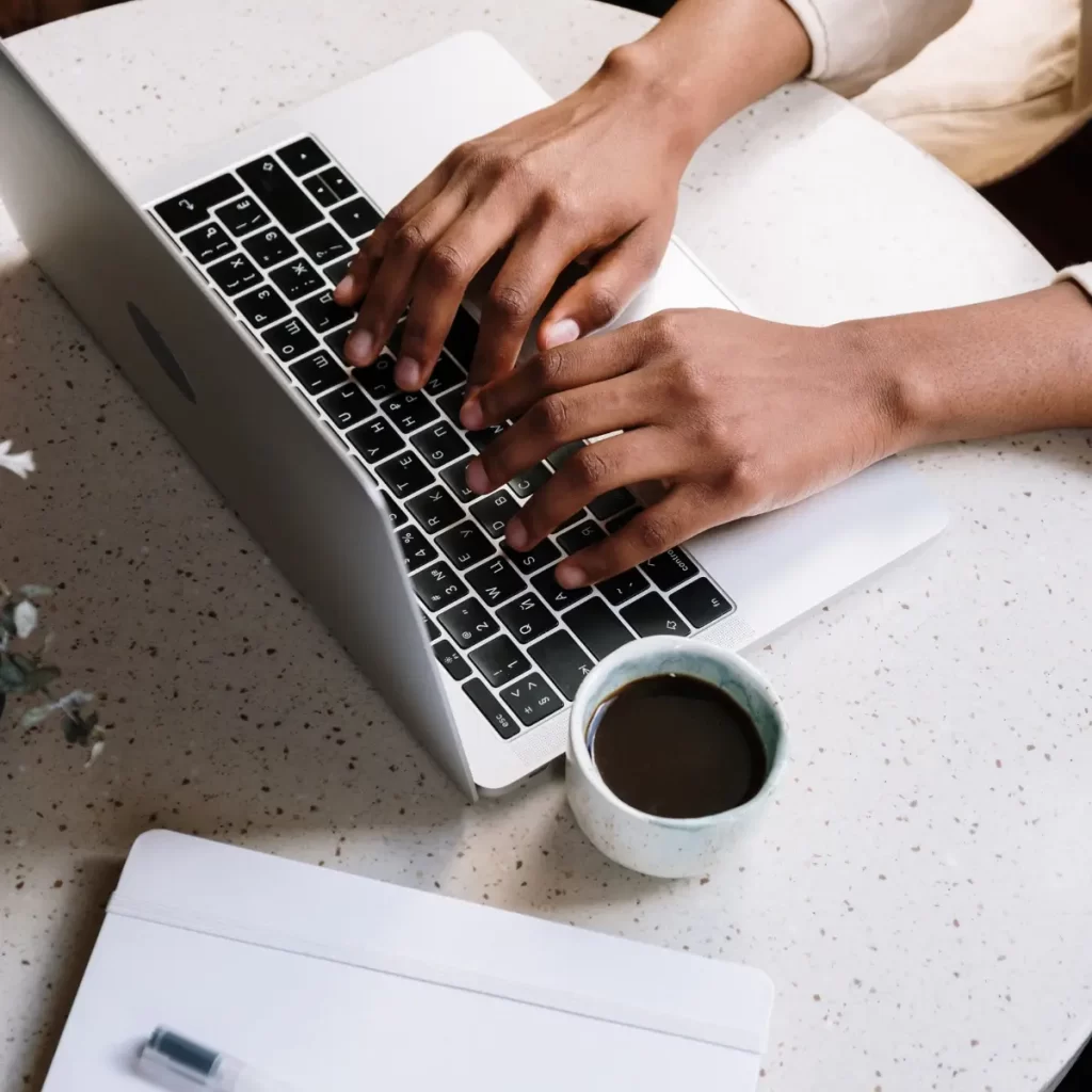 Una persona escribiendo en su pc y una taza de café al lado.